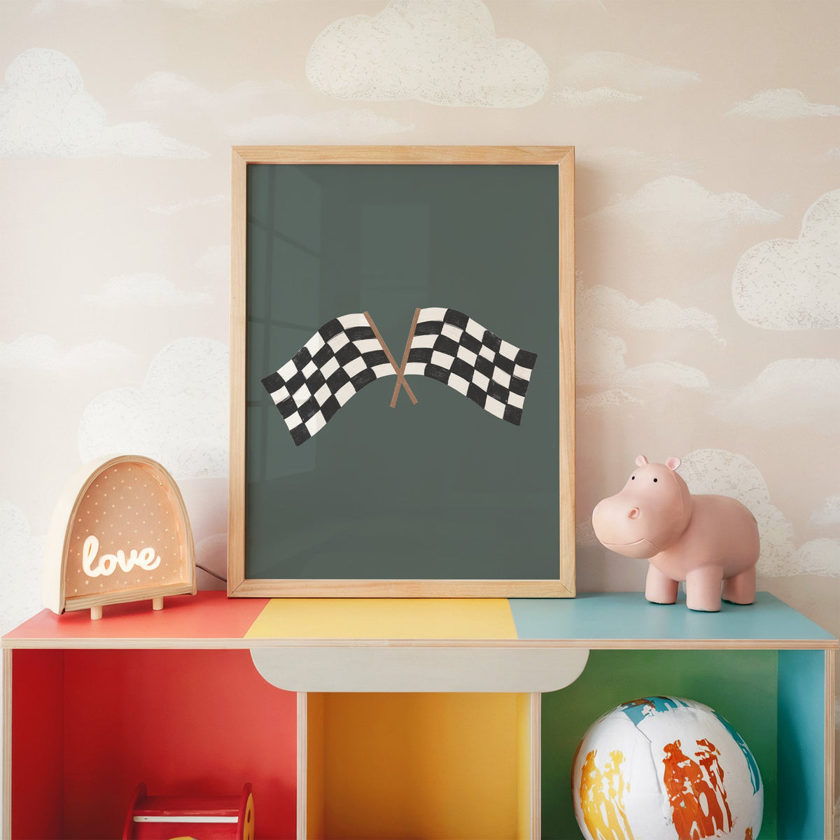 Crossed checkered racing flags nursery print in an oak frame on a rainbow toy shelf against cloud wallpaper