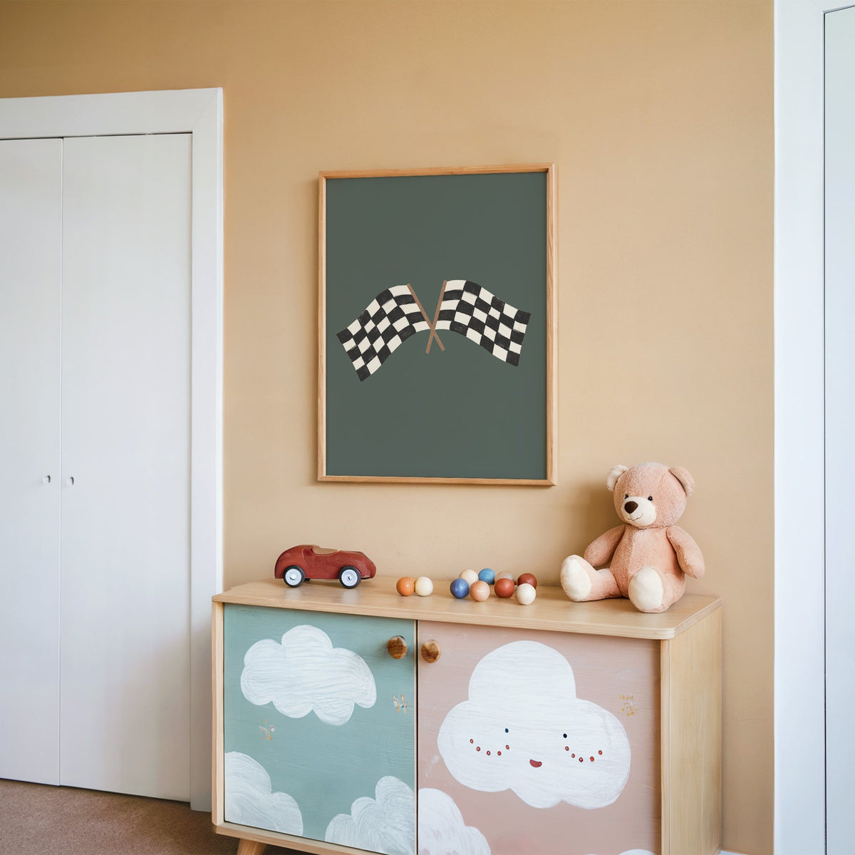 Crossed checkered racing flags nursery print in an oak frame on a peach wall above a cloud-painted cabinet