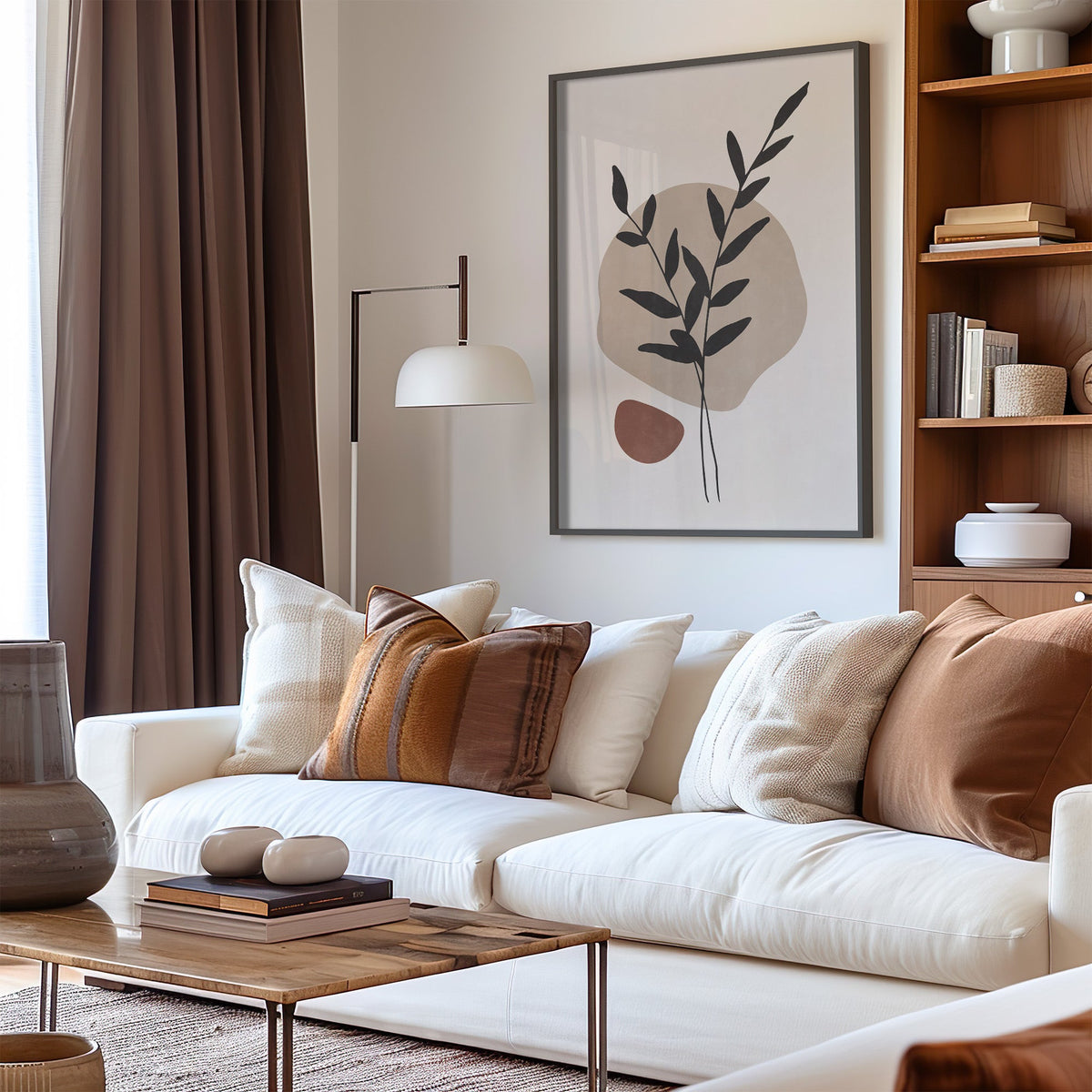 Crossed leaf stems and rust pebble botanical print in a black frame above a cream sofa with brown striped pillows