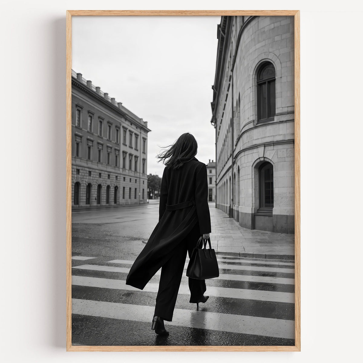 Woman in long black coat on wet crosswalk print in a light oak frame on a plain white wall