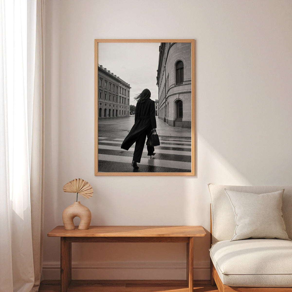 Woman in long black coat on wet crosswalk print in an oak frame above a narrow console with an arched vase