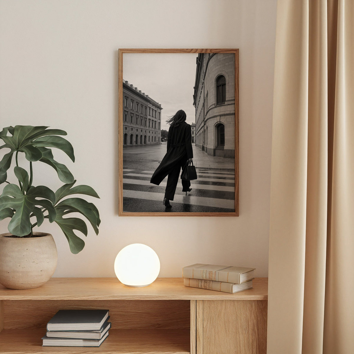 Woman in long black coat on wet crosswalk print in a walnut frame above an oak cabinet with a glowing globe lamp