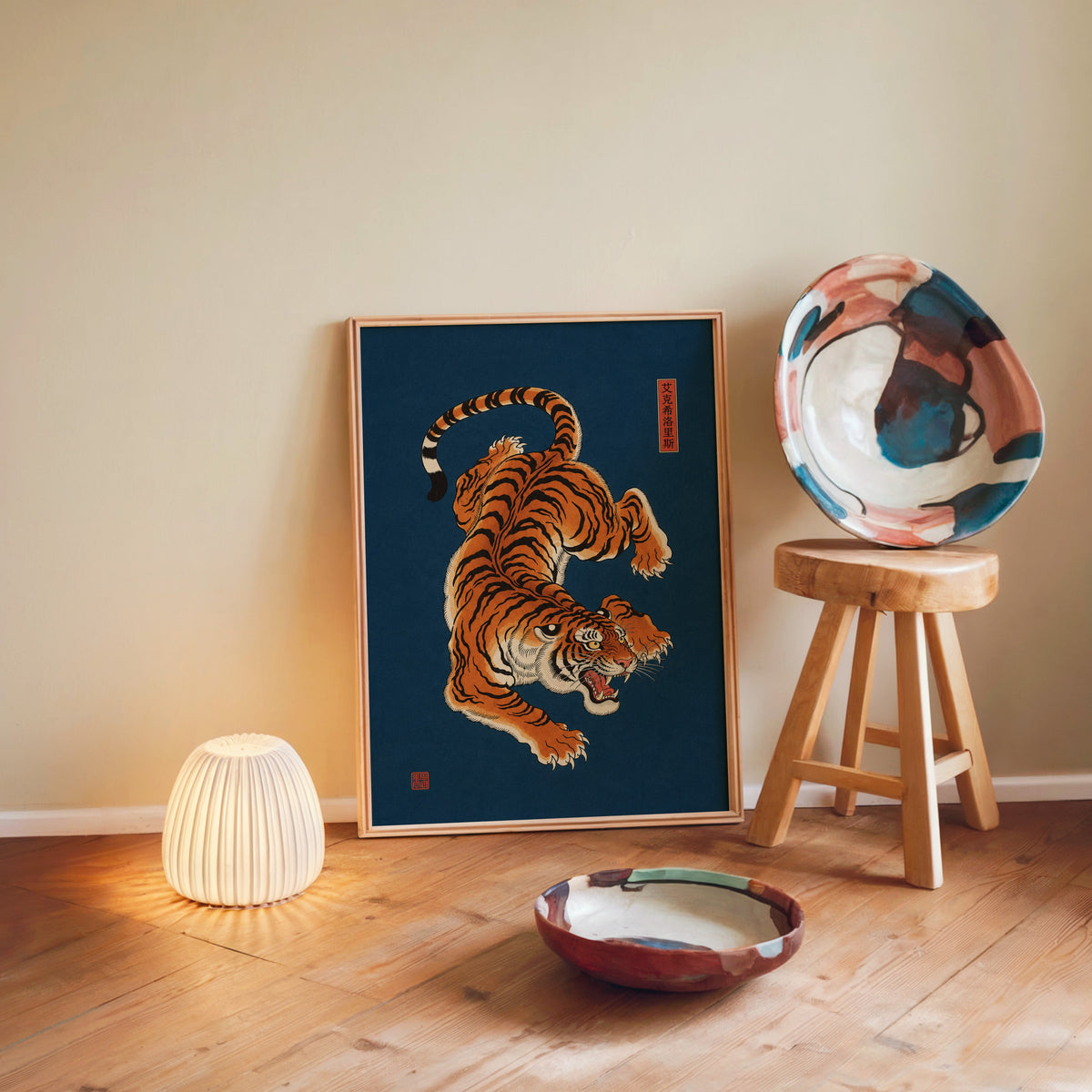 orange tiger on navy blue print in a light wood frame leaning on a wooden floor by a glowing lamp and stool