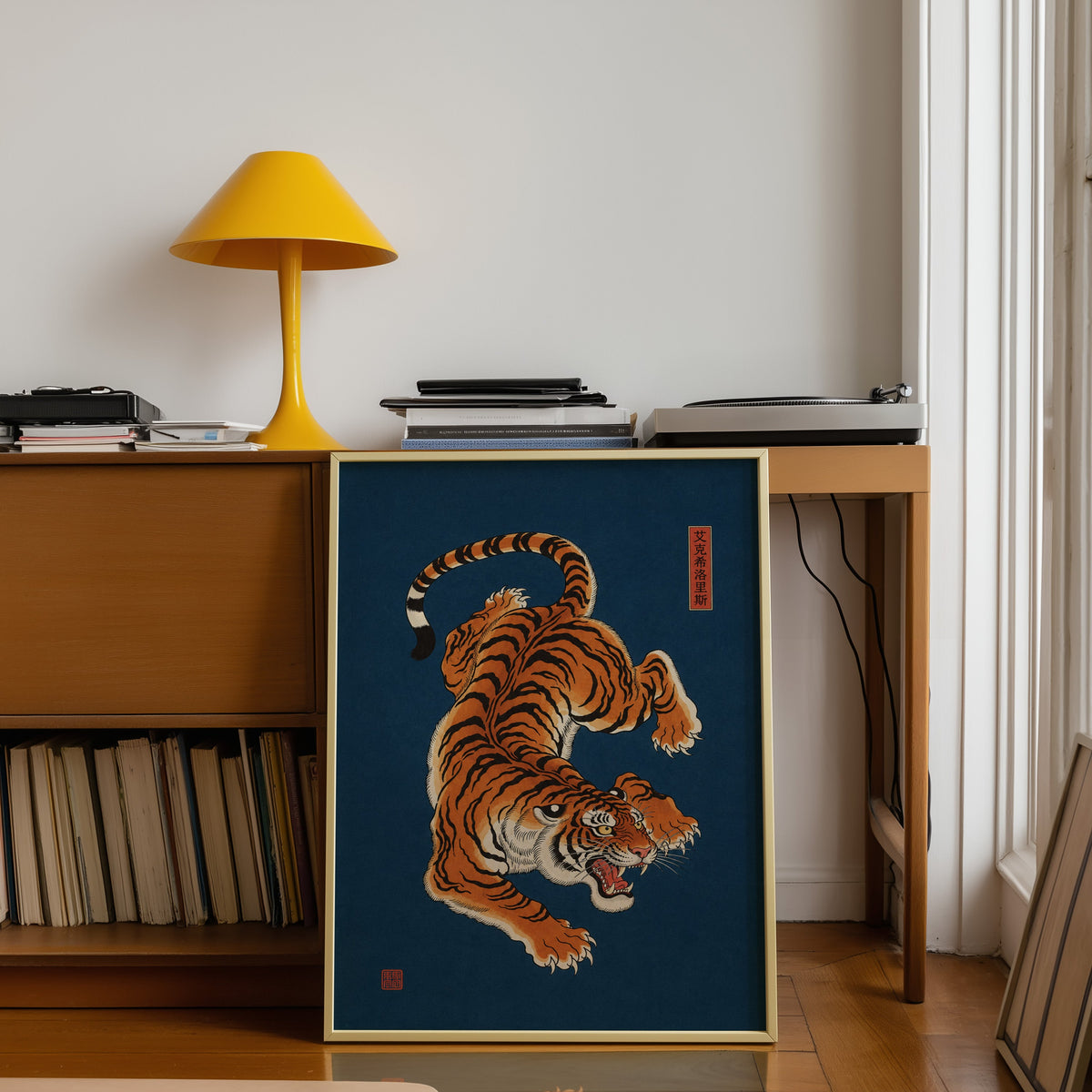 orange tiger on navy blue print shown in a gold frame leaning under a teak desk with a yellow lamp