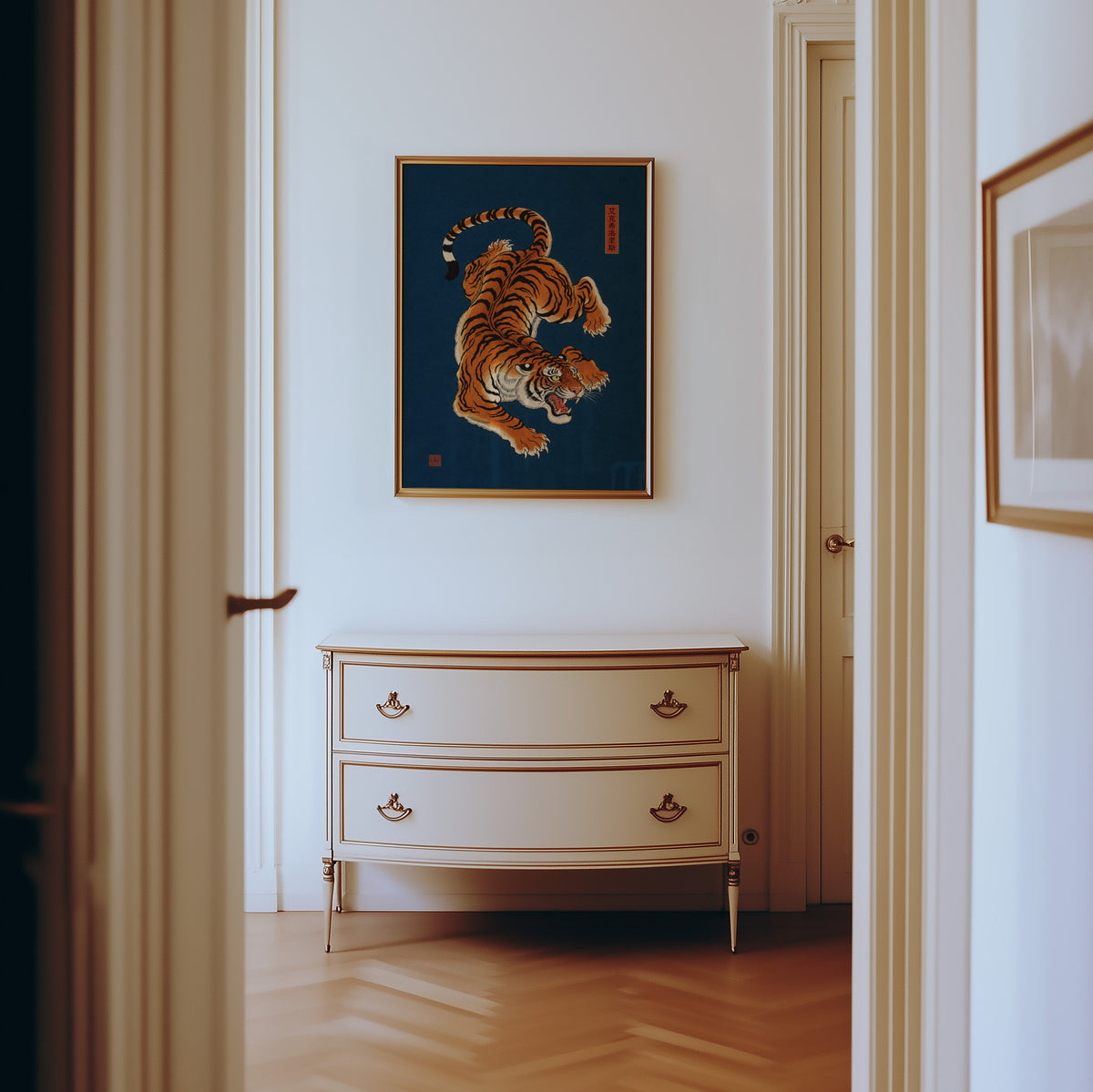 orange tiger on navy blue print shown in a gold frame in a hallway above a cream dresser