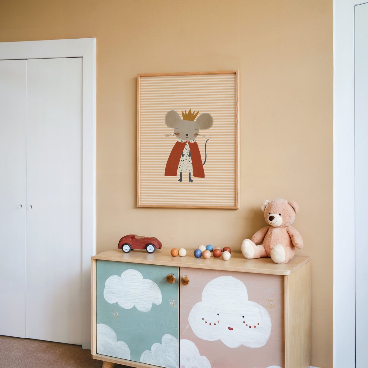 Crowned mouse red cape nursery print in an oak frame on a peach wall above a cloud-painted cabinet