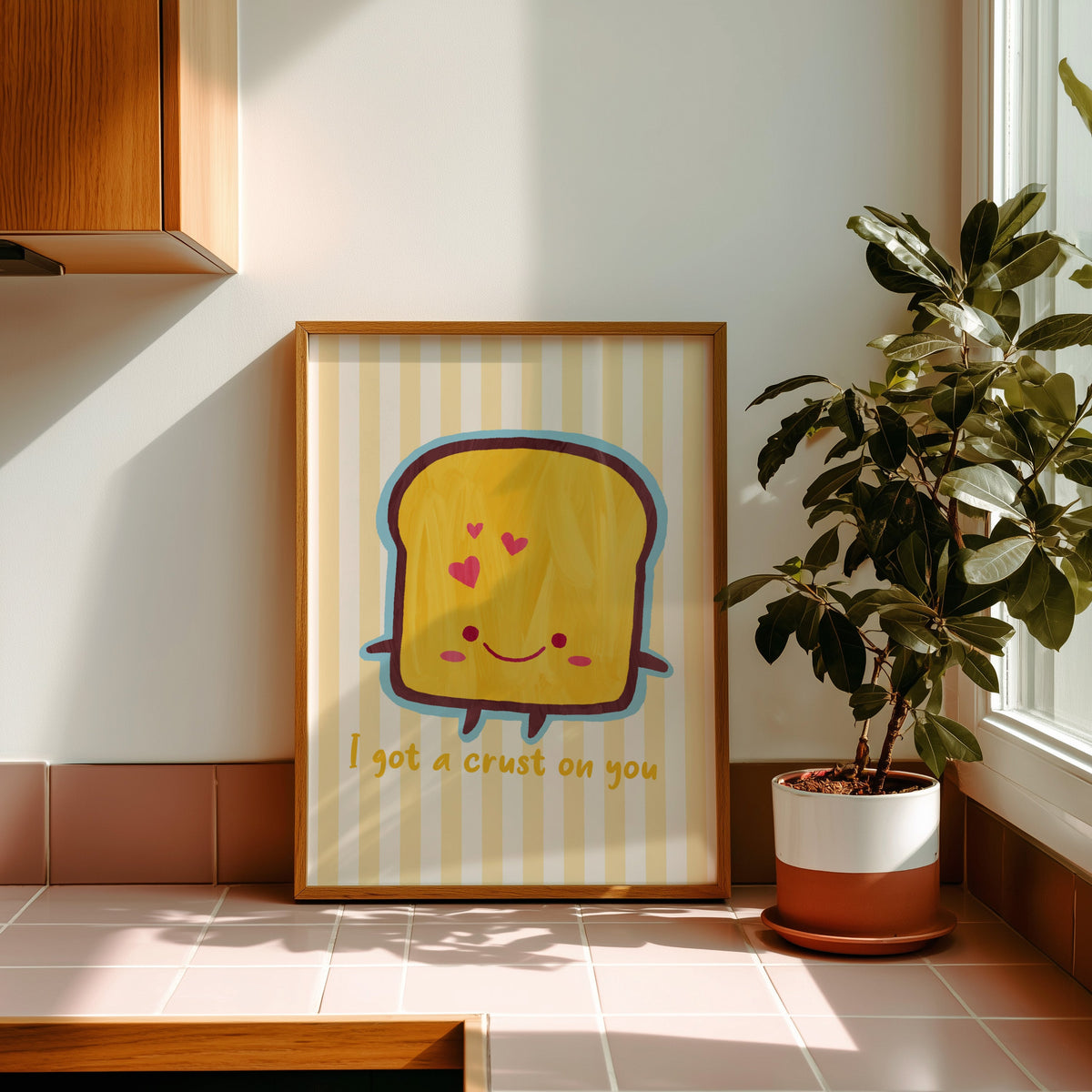 I got a crust on you smiling toast print in a golden oak frame leaning on a pink tiled ledge in strong afternoon sun