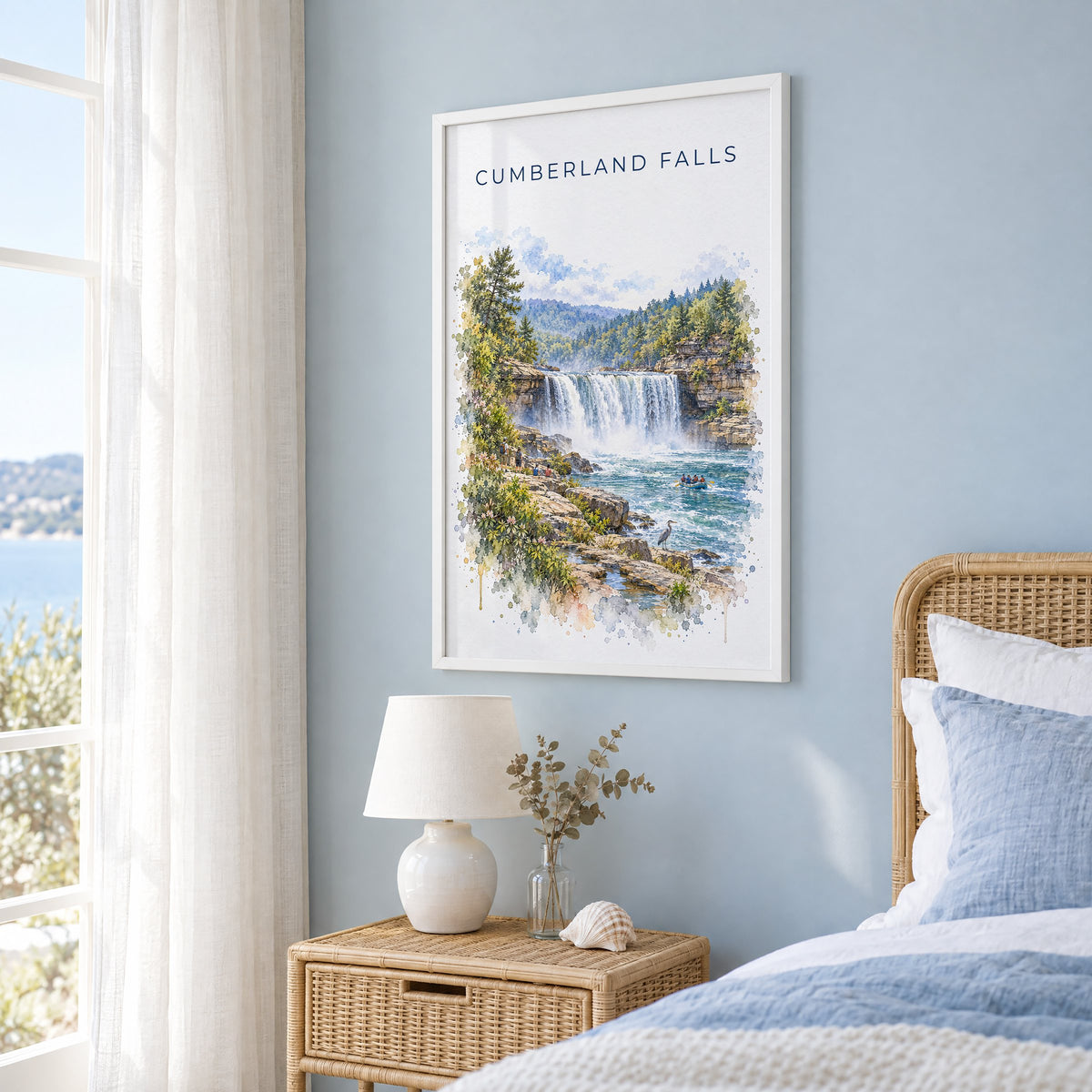 Cumberland Falls watercolor print in a white frame on a pale blue wall beside a rattan bed in a coastal bedroom