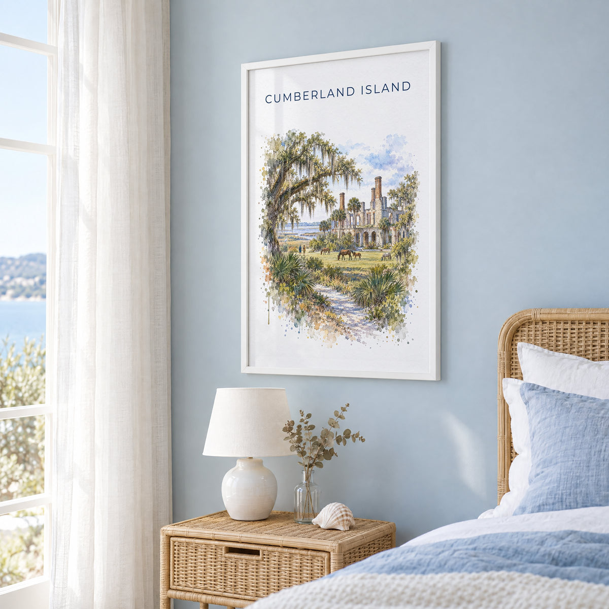 Cumberland Island watercolor print in a white frame on a pale blue wall beside a rattan bed in a coastal bedroom
