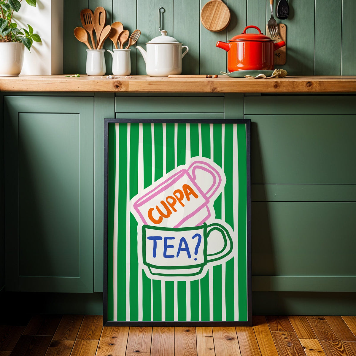 Cuppa tea print in a black frame against sage green kitchen cabinets