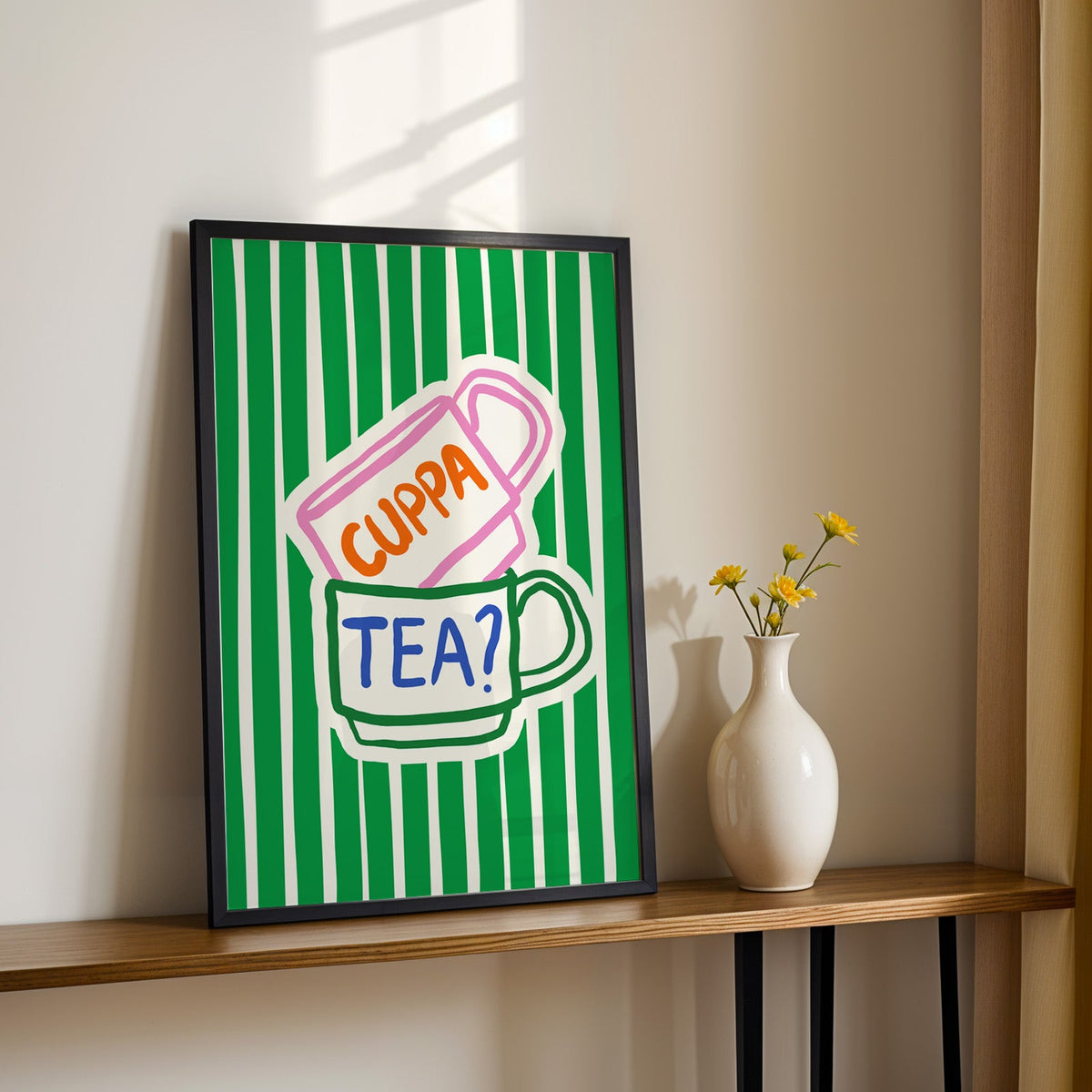 Cuppa tea print in a black frame on a console table with yellow daisies