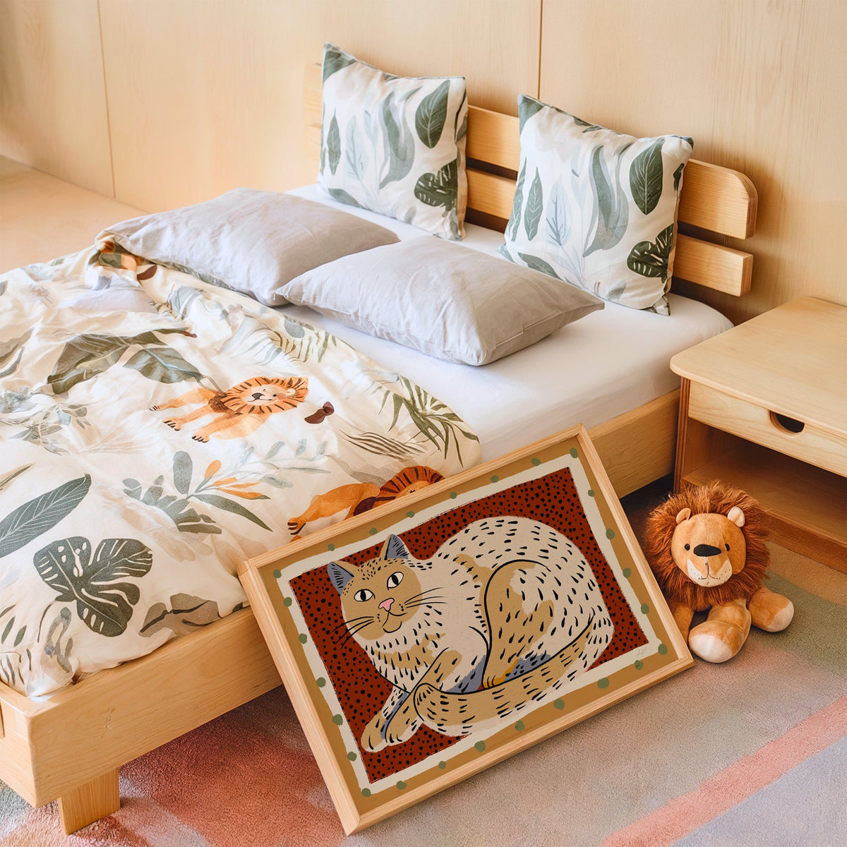 Curled cream cat on rust dots nursery print in an oak frame leaning on a kids bed by a lion plush