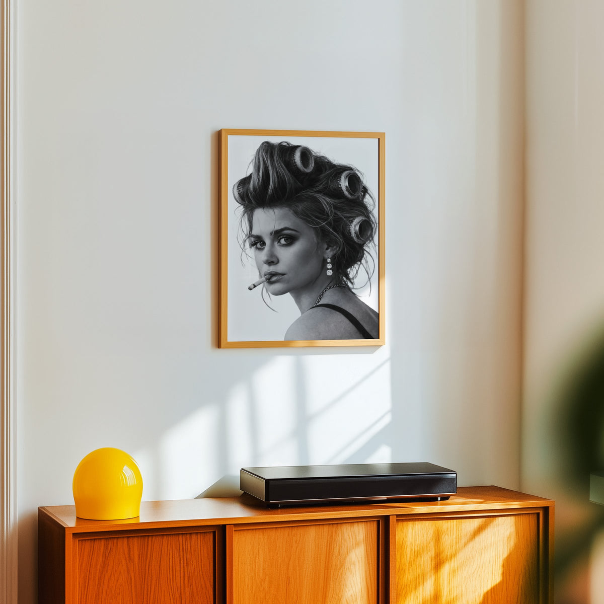 Woman in big curlers looking over shoulder print in an oak frame above a teak sideboard with a yellow glass lamp
