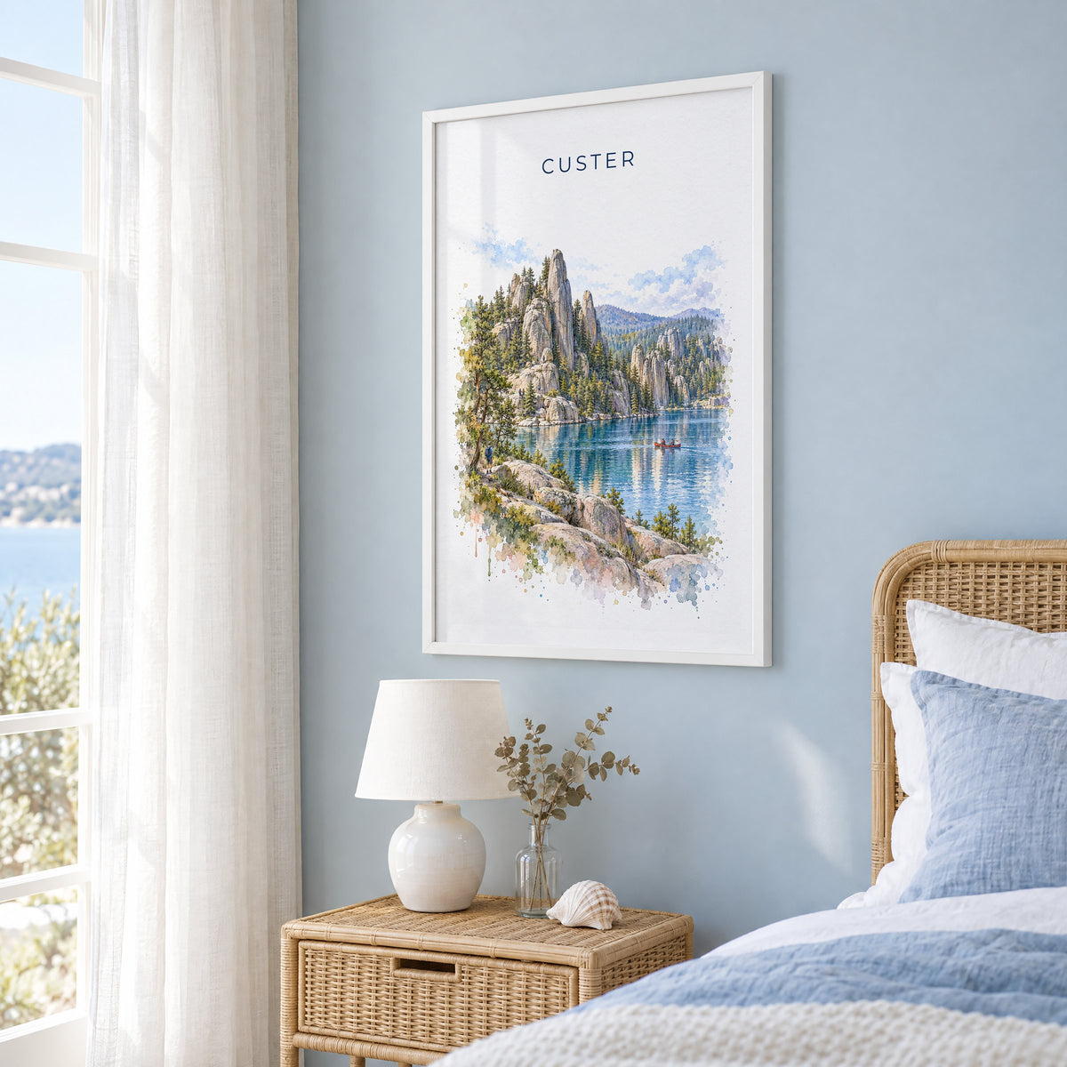 Custer State Park watercolor print in a white frame on a pale blue wall beside a rattan bed in a coastal bedroom