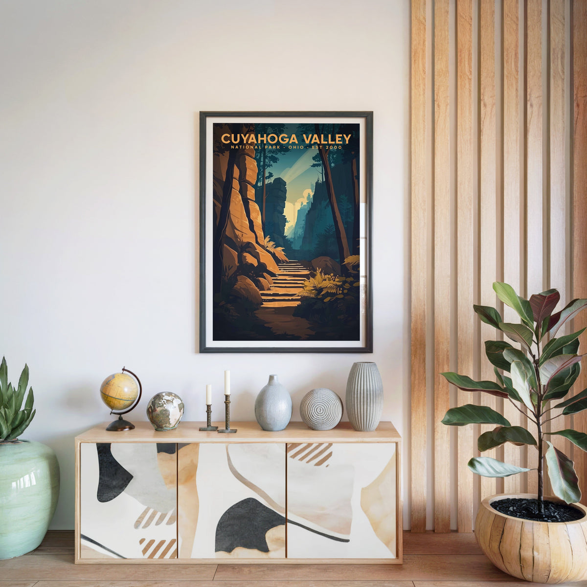 Cuyahoga Valley print in a black frame above a light wood sideboard with a globe and vases