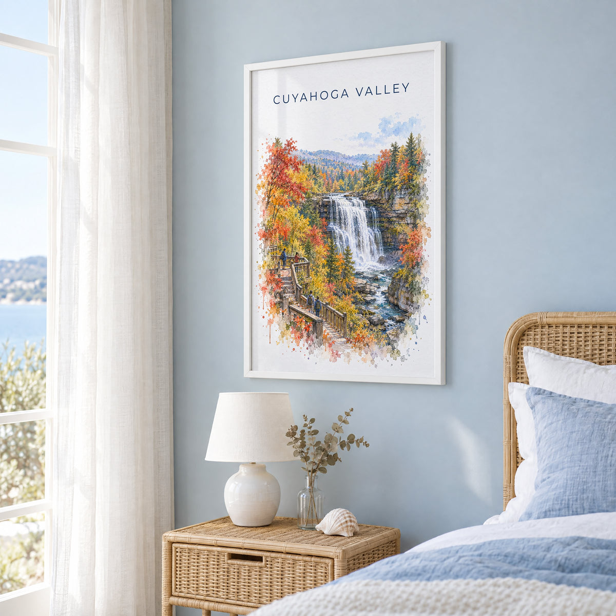Cuyahoga Valley National Park watercolor print in a white frame on a pale blue wall beside a rattan bed in a coastal bedroom