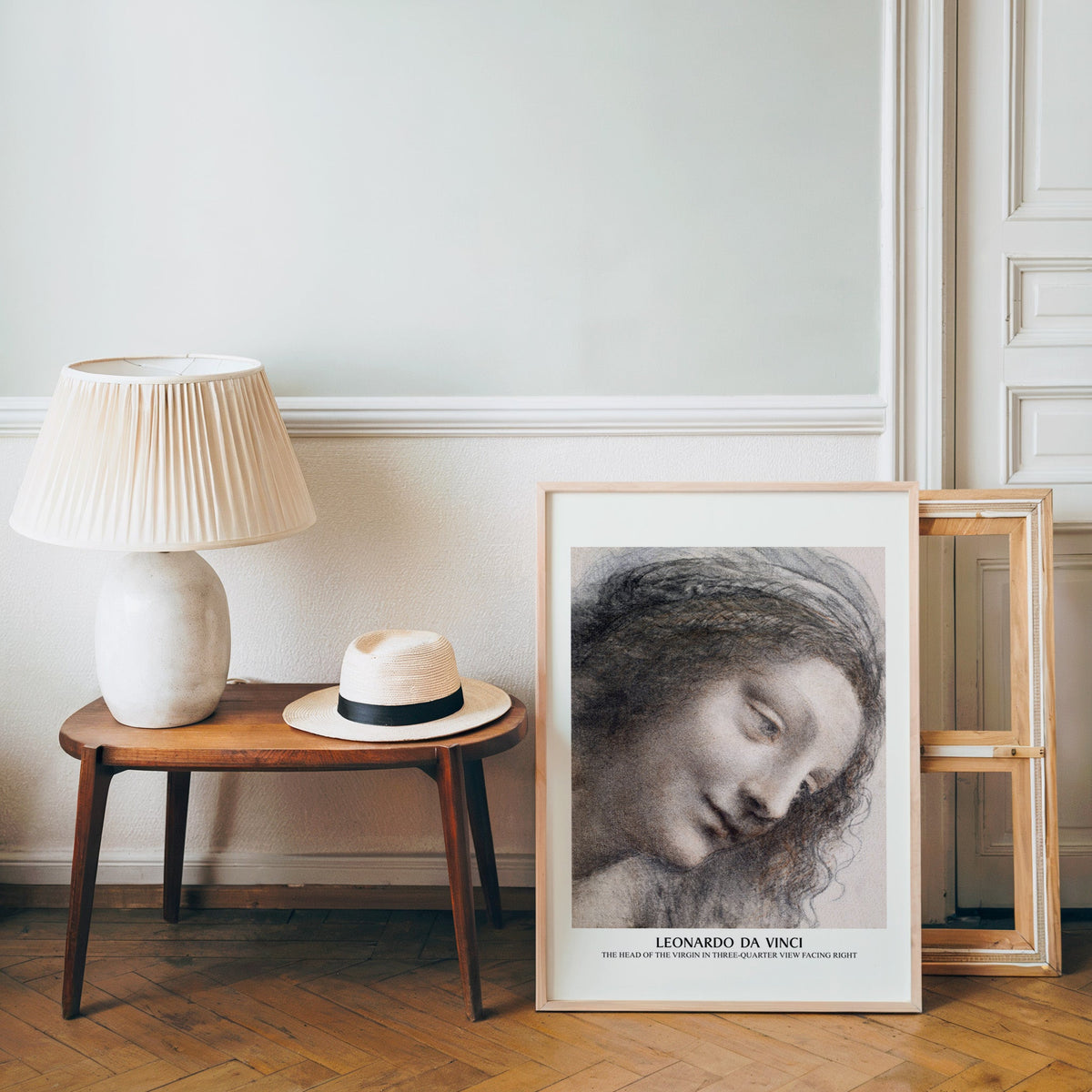 Old master sketch poster in a light wood frame leaning by a bench and hat