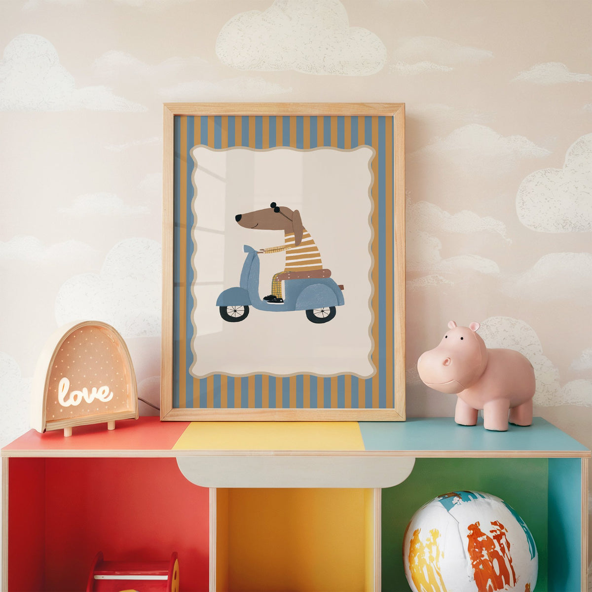 Dachshund on blue scooter nursery print in an oak frame on a rainbow toy shelf against cloud wallpaper