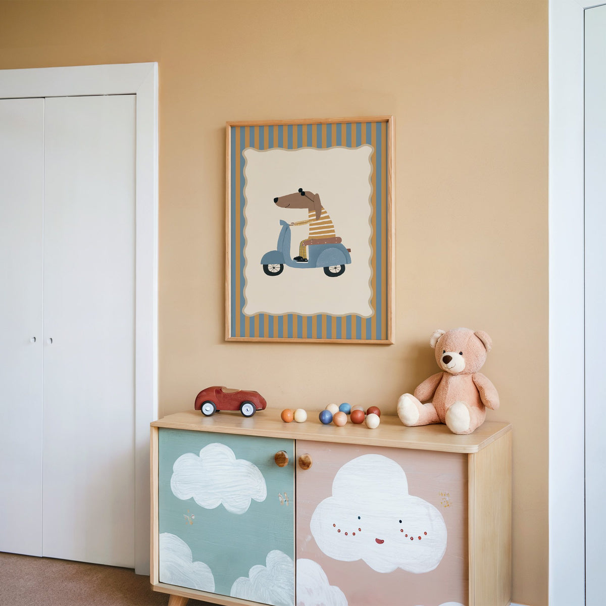 Dachshund on blue scooter nursery print in an oak frame on a peach wall above a cloud-painted cabinet