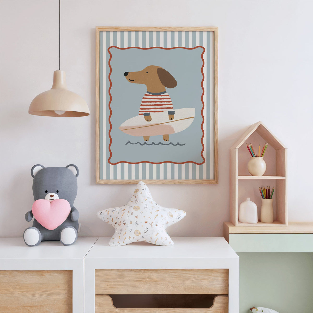 Dachshund holding surfboard nursery print in an oak frame above a white dresser with a star pillow and house shelf