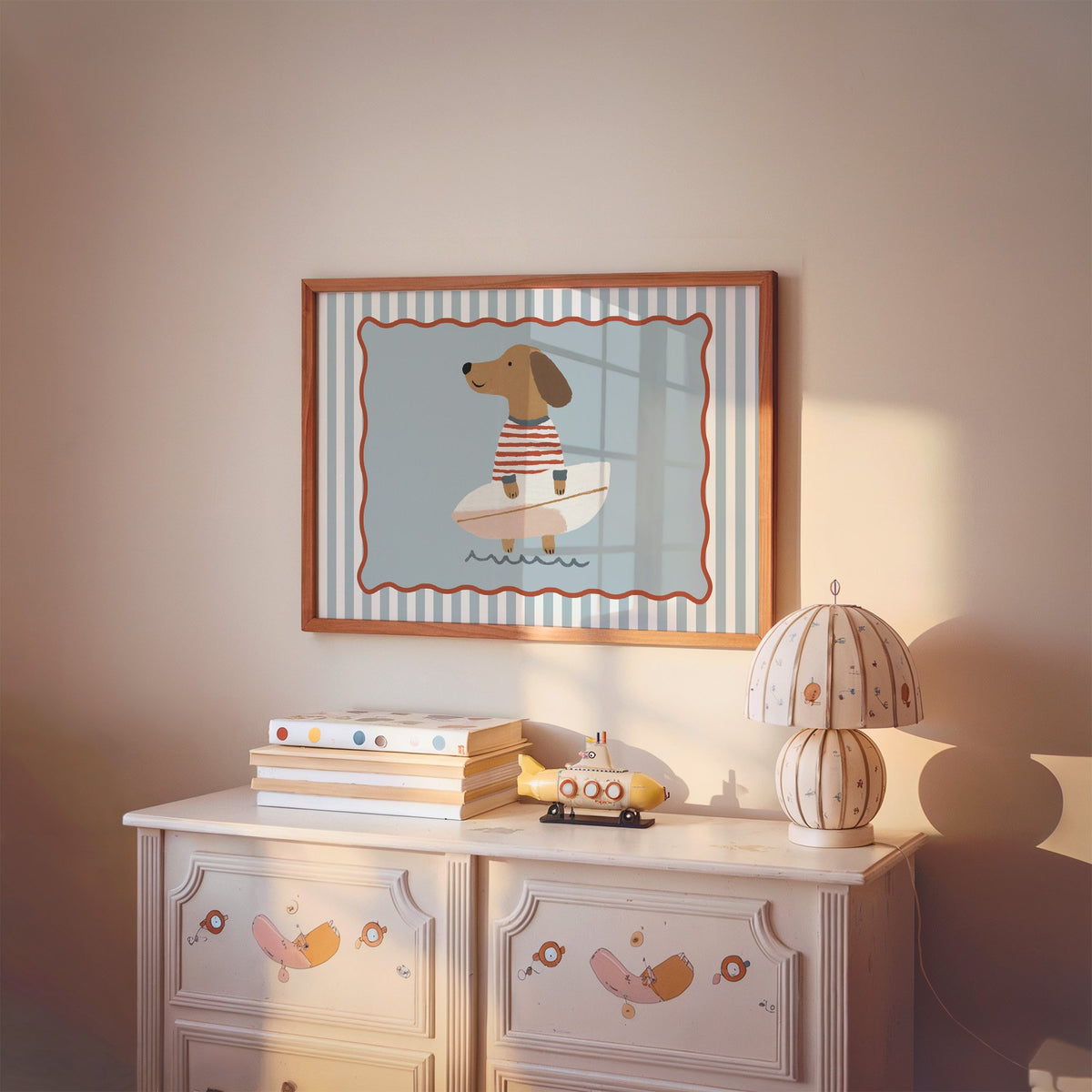 Landscape dachshund holding surfboard nursery print in a cherry wood frame above a painted dresser and lamp