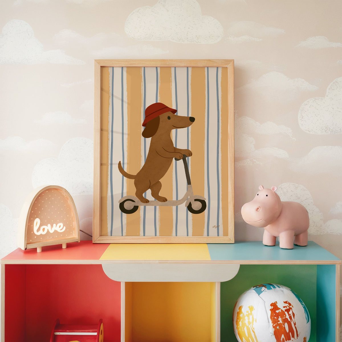 Dachshund riding scooter on stripes nursery print in an oak frame on a rainbow toy shelf against cloud wallpaper