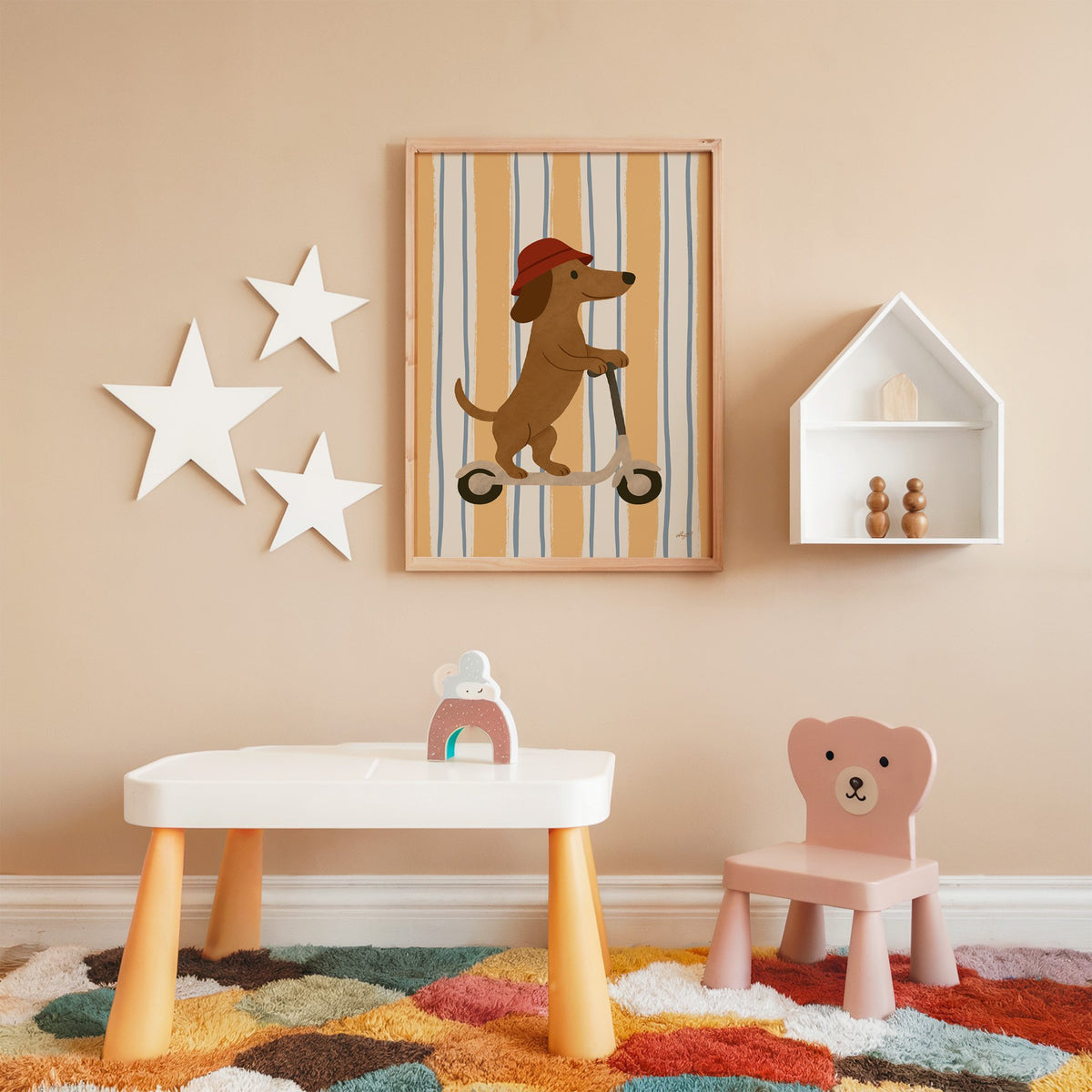 Dachshund riding scooter on stripes nursery print in an oak frame on a peach wall above a kids table with wall stars