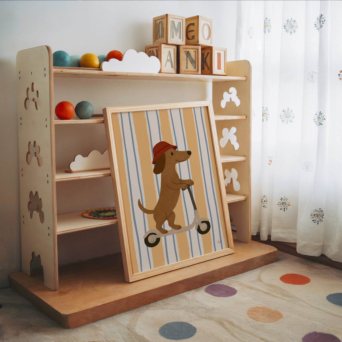 Dachshund riding scooter on stripes nursery print in an oak frame leaning on a toy shelf with wooden letter blocks