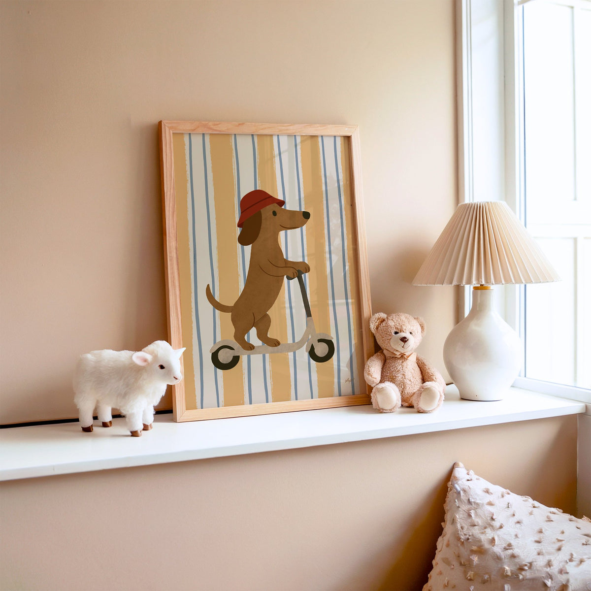 Dachshund riding scooter on stripes nursery print in an oak frame on a window ledge with a toy lamb and teddy