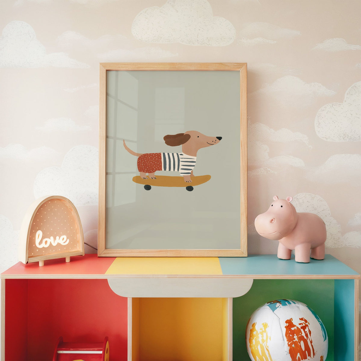 Dachshund skateboard sage nursery print in an oak frame on a rainbow toy shelf against cloud wallpaper