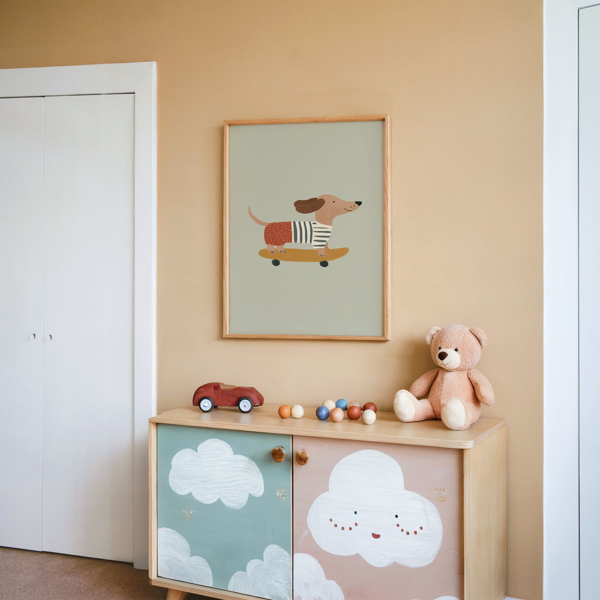 Dachshund skateboard sage nursery print in an oak frame on a peach wall above a cloud-painted cabinet