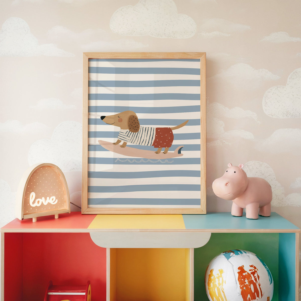 Dachshund on pink surfboard nursery print in an oak frame on a rainbow toy shelf against cloud wallpaper