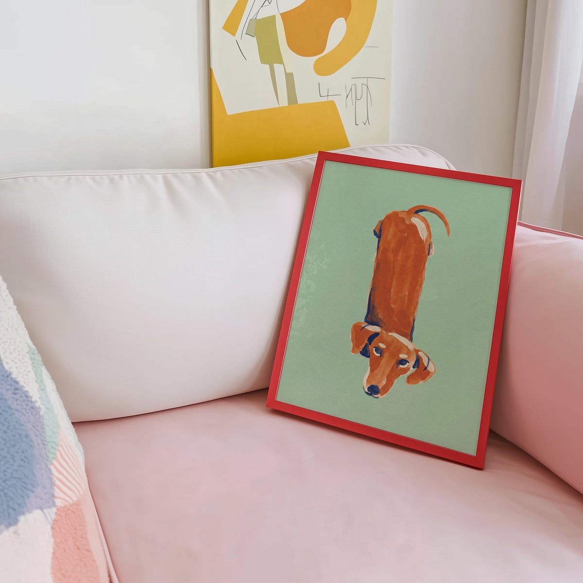 Top-down dog print shown in a red frame leaning on a blush pink sofa