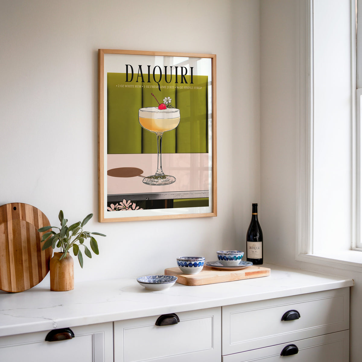Daiquiri recipe print in an oak frame above a white sideboard with a bottle of wine