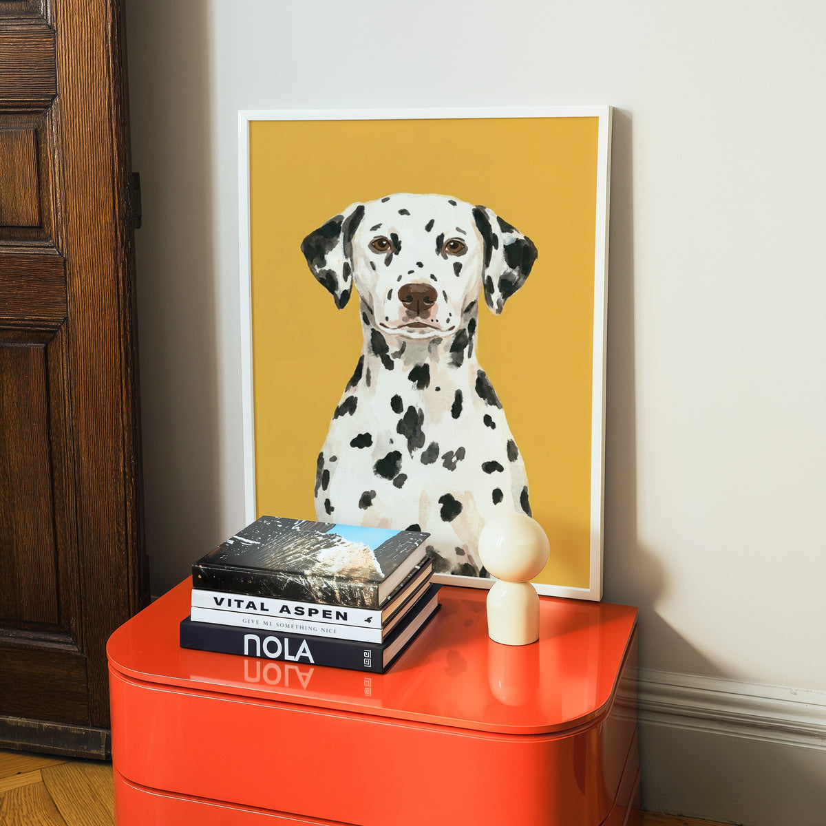 Watercolor Dalmatian print in a white frame on a glossy orange cabinet with books