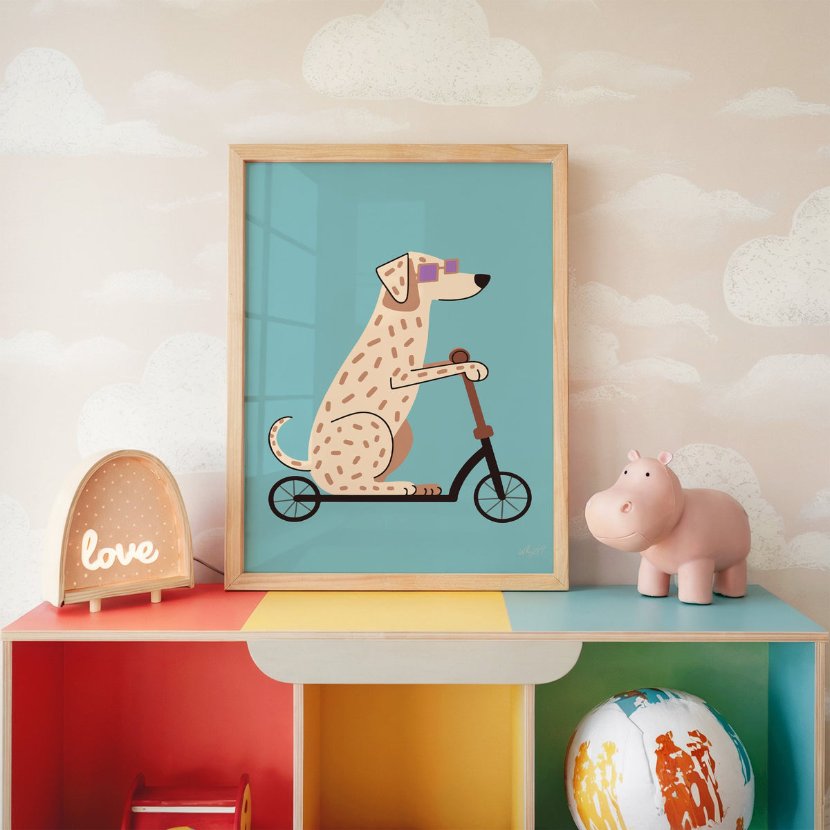 Dalmatian on scooter with purple glasses nursery print in an oak frame on a rainbow toy shelf against cloud wallpaper