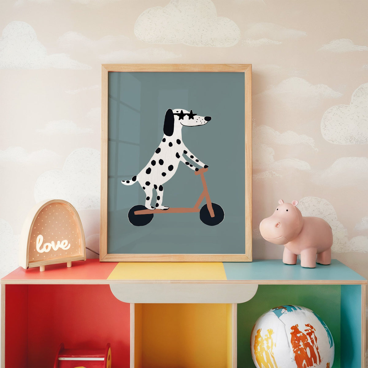 Dalmatian on scooter star glasses nursery print in an oak frame on a rainbow toy shelf against cloud wallpaper