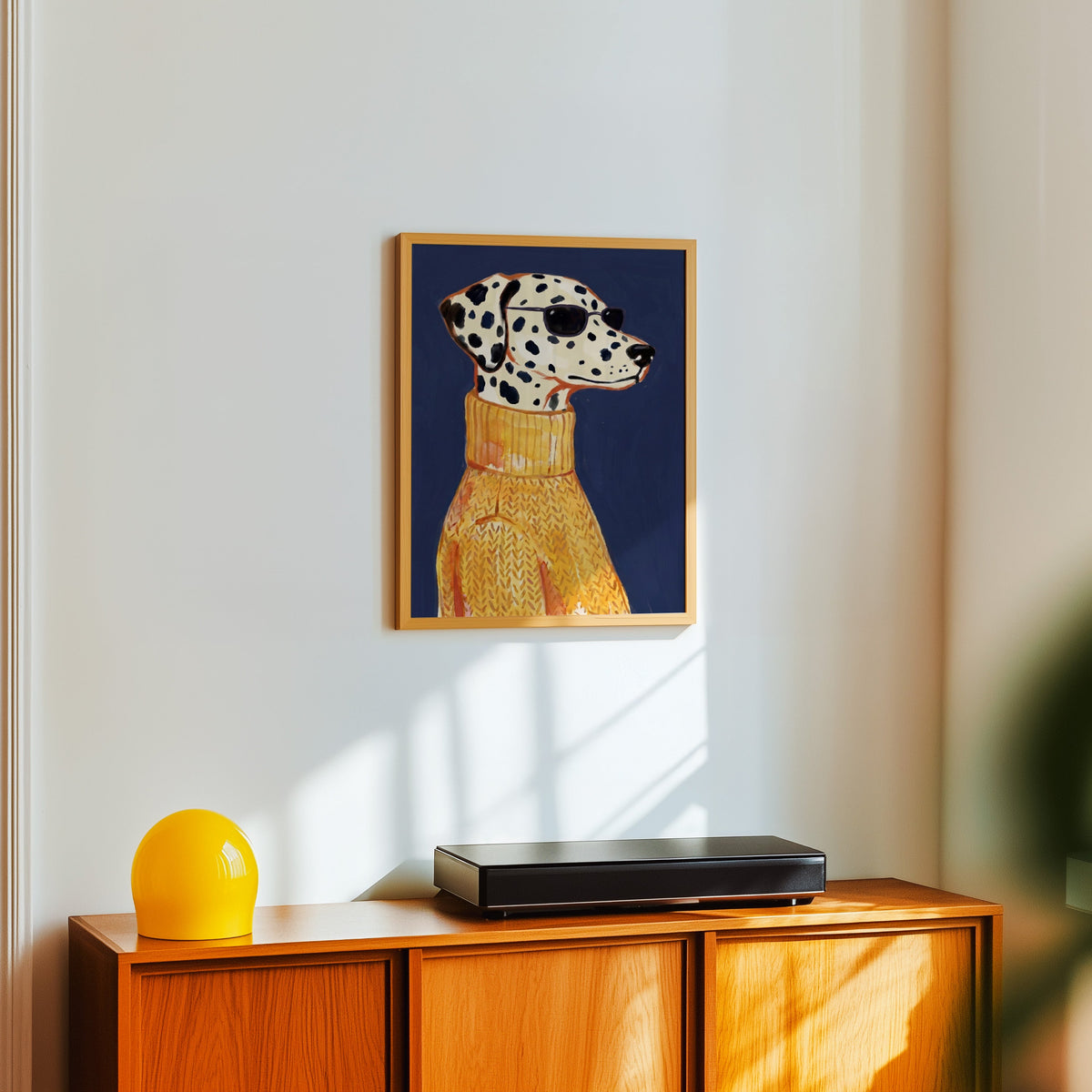 Navy and mustard dog print in a light oak frame above a teak sideboard with a yellow lamp