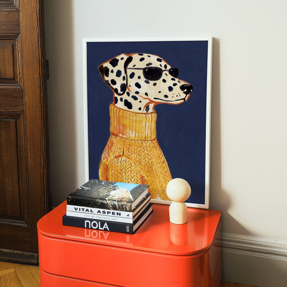 Dog in yellow sweater print in a white frame on a glossy orange cabinet with books