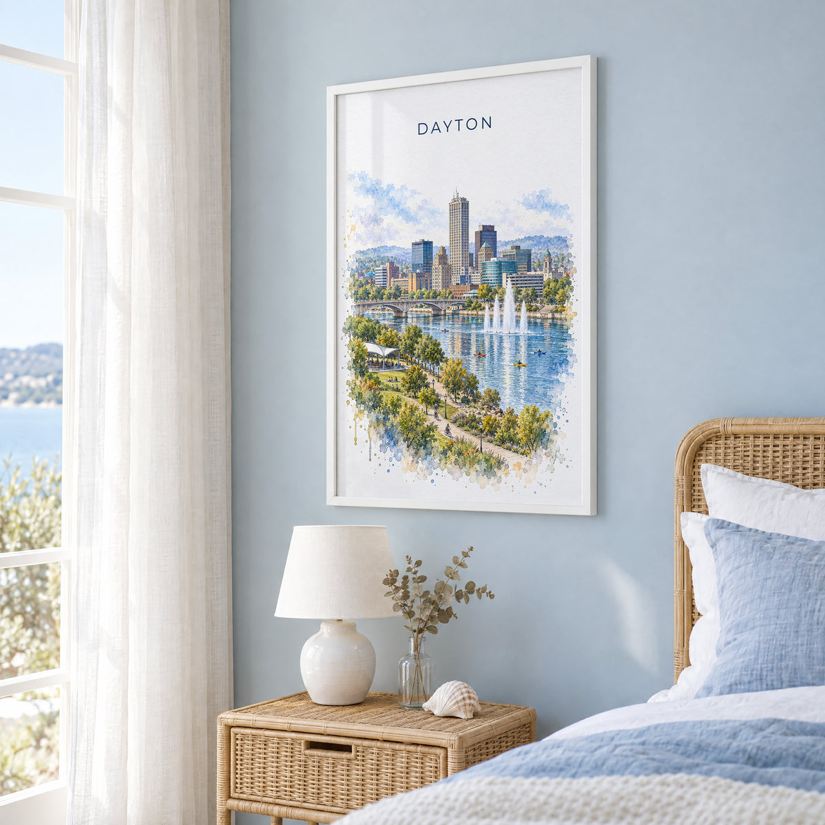 Dayton, Ohio watercolor print in a white frame on a pale blue wall beside a rattan bed in a coastal bedroom