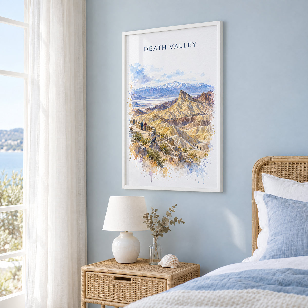 Death Valley National Park watercolor print in a white frame on a pale blue wall beside a rattan bed in a coastal bedroom