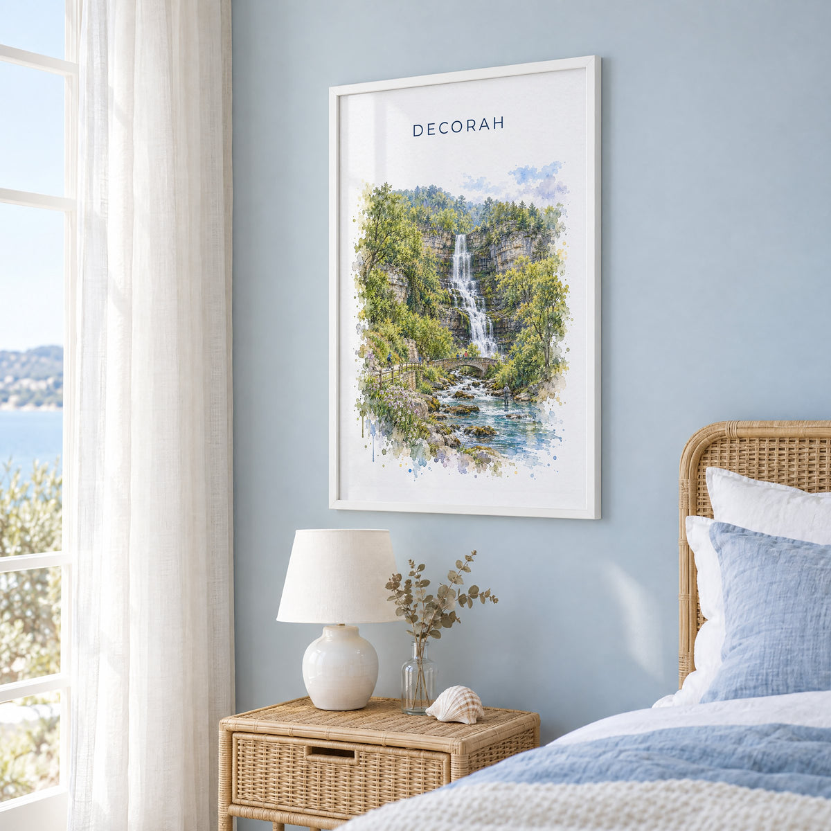 Decorah, Iowa watercolor print in a white frame on a pale blue wall beside a rattan bed in a coastal bedroom