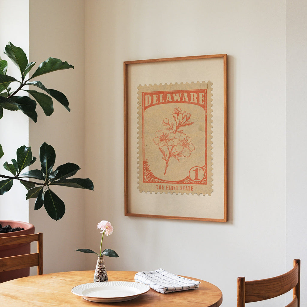 Delaware state flower print framed above a round wooden table with a single bloom in a vase and books