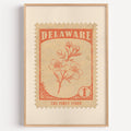Delaware state flower stamp print in orange red on sand, light oak frame on a plain white wall