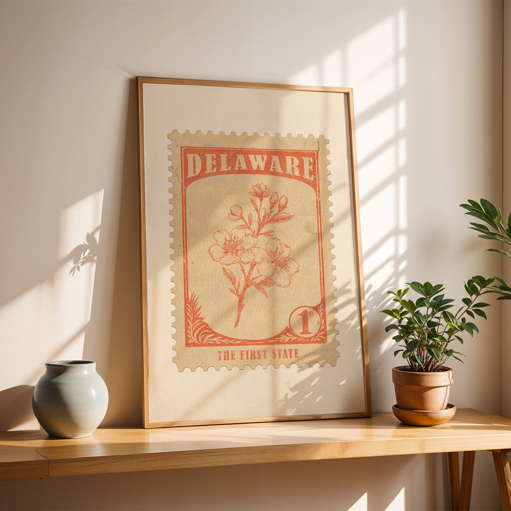 Delaware peach blossom stamp print in a light oak frame leaning on a wooden table beside a stoneware vase