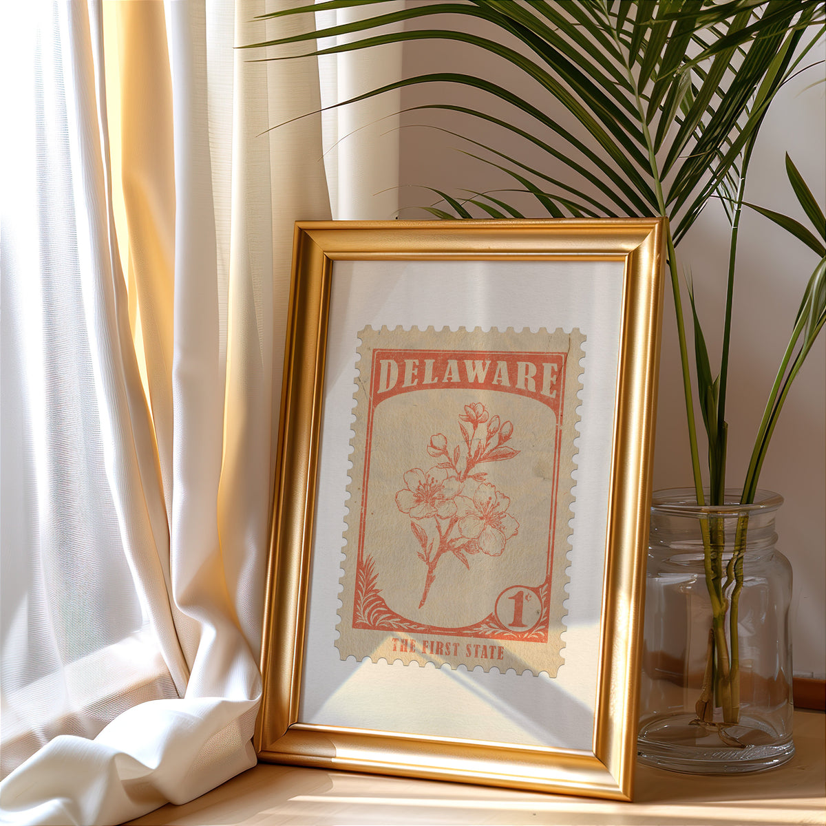 Delaware stamp print in a gold frame leaning by a cream curtain with a palm in a glass jar