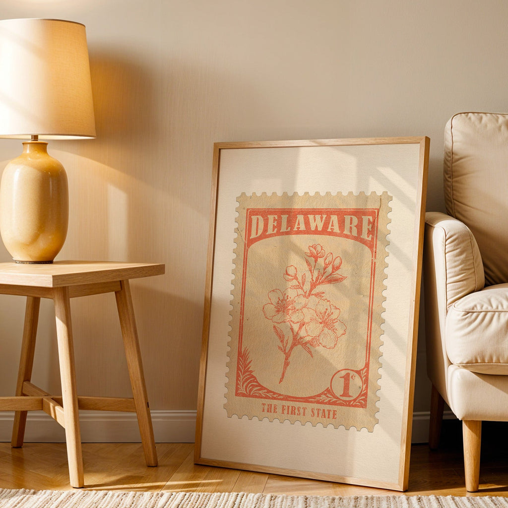 Delaware stamp print in a wood frame resting on the floor beside a beige armchair and a yellow lamp
