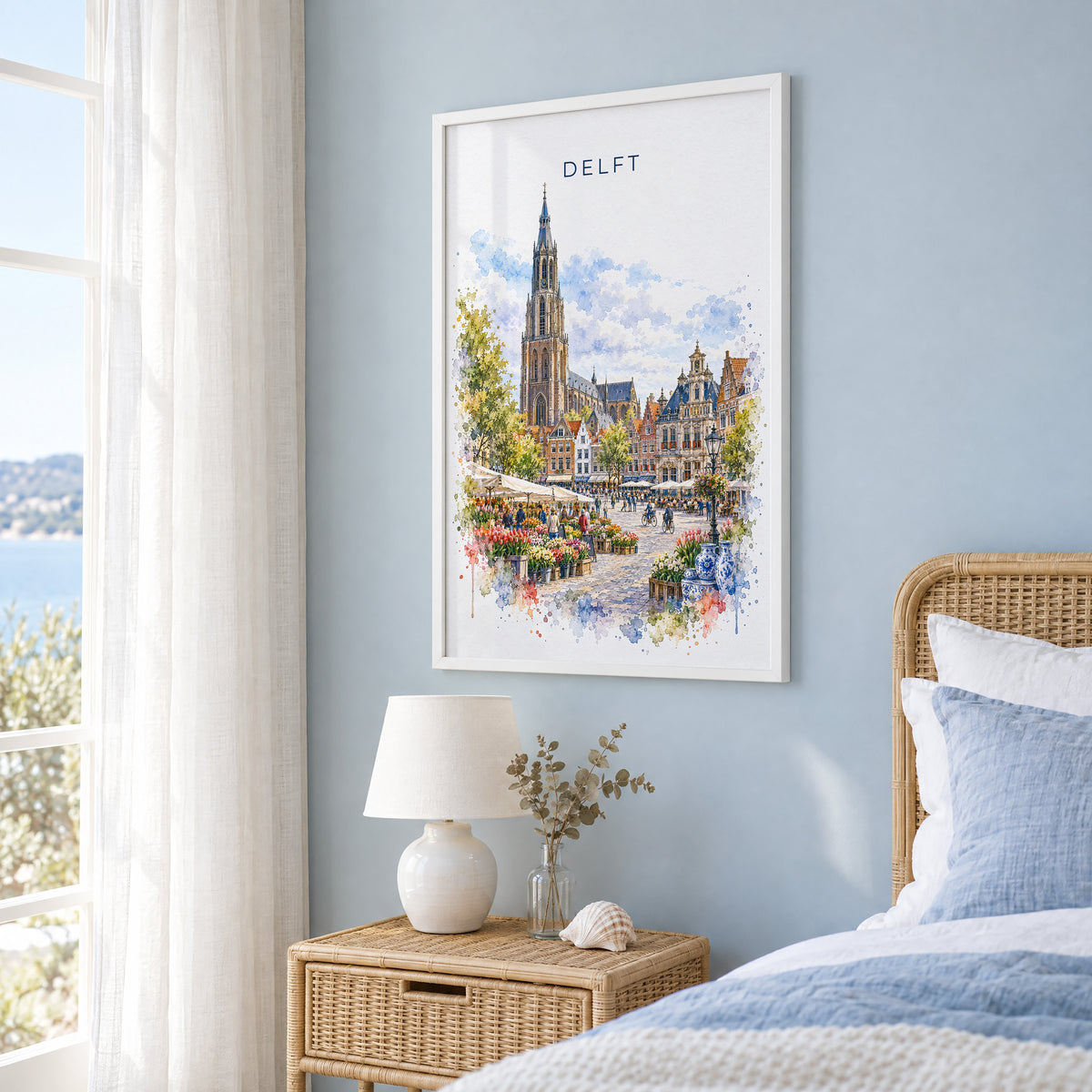 Delft watercolor print in a white frame on a pale blue wall beside a rattan bed in a coastal bedroom