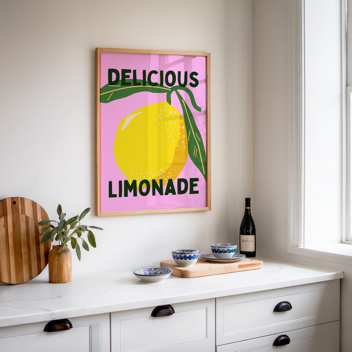 Delicious Limonade print in an oak frame above a white sideboard with a bottle of wine