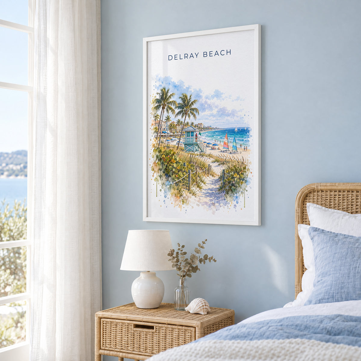 Delray Beach watercolor print in a white frame on a pale blue wall beside a rattan bed in a coastal bedroom